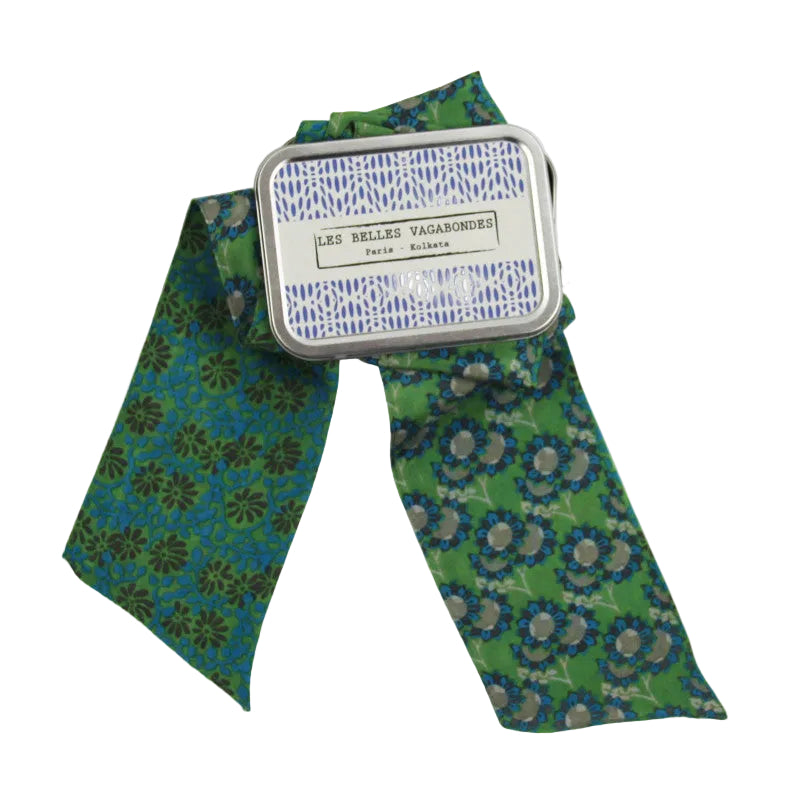 A green patterned necktie with blue and gray floral motifs, tied with a silver metal ribbon that has a white paper label reading 'LES BELLES VAGABONDES France Allemande'.