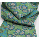 A folded piece of green fabric with a repeating floral pattern in blue, gray, and olive green, shown on a plain white background.