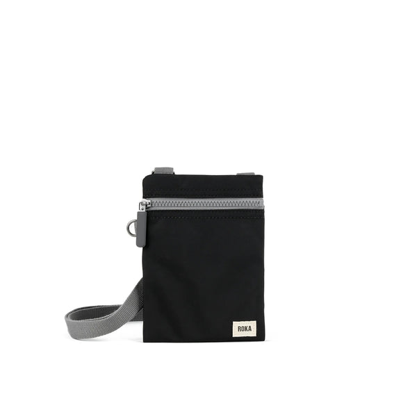 A photo of the front of a small rectangular black pocket bag. It has a grey zip horizontally at the top, grey straps, and a small ROKA logo in the bottom right corner.