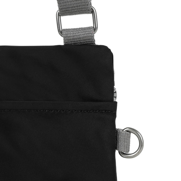 A close up photo of the back of a black bag, showing the grey strap and neatly stitched pocket opening.
