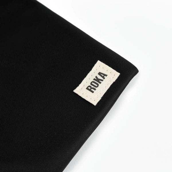 A close up photo of the bottom corner of a black bag, showing the ROKA London label.