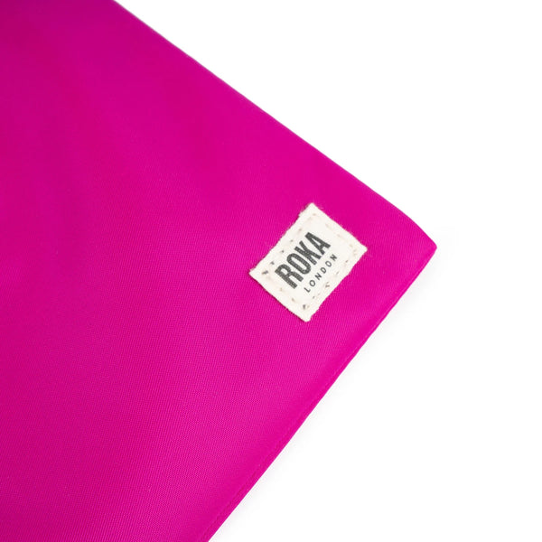 A close up photo of the bottom corner of a bright pink bag, showing the ROKA London label.