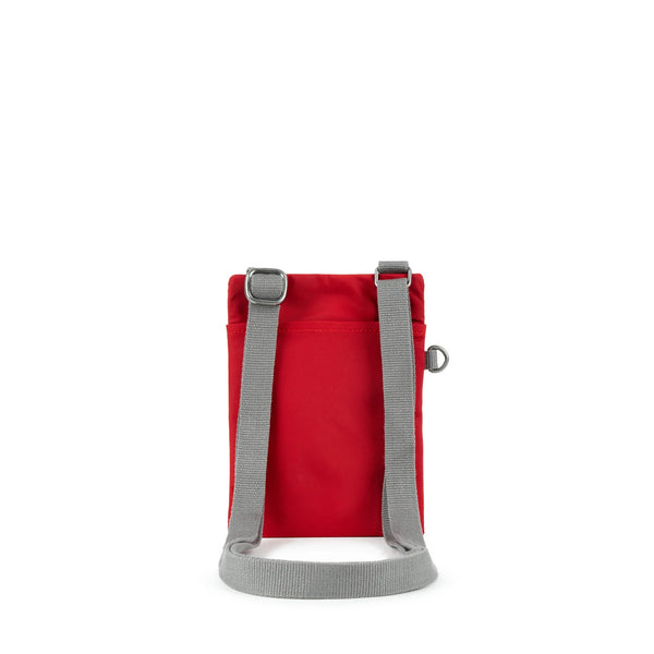 A photo of the back of a small rectangular red pocket bag. It has a pocket and grey straps.