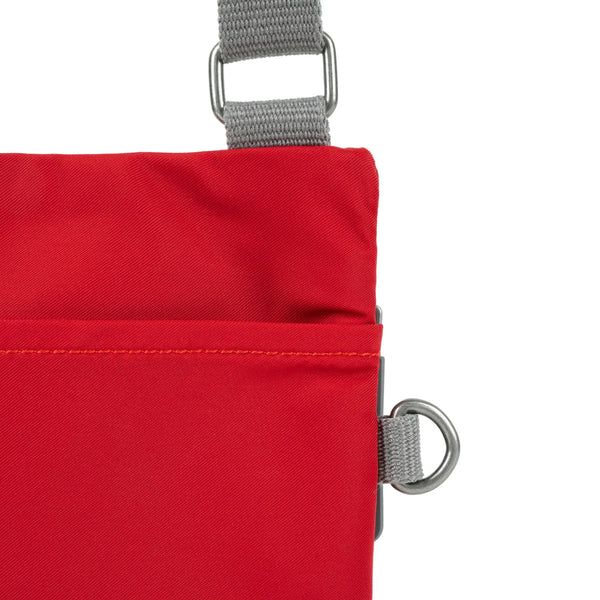 A close up photo of the back of a red bag, showing the grey strap and neatly stitched pocket opening.