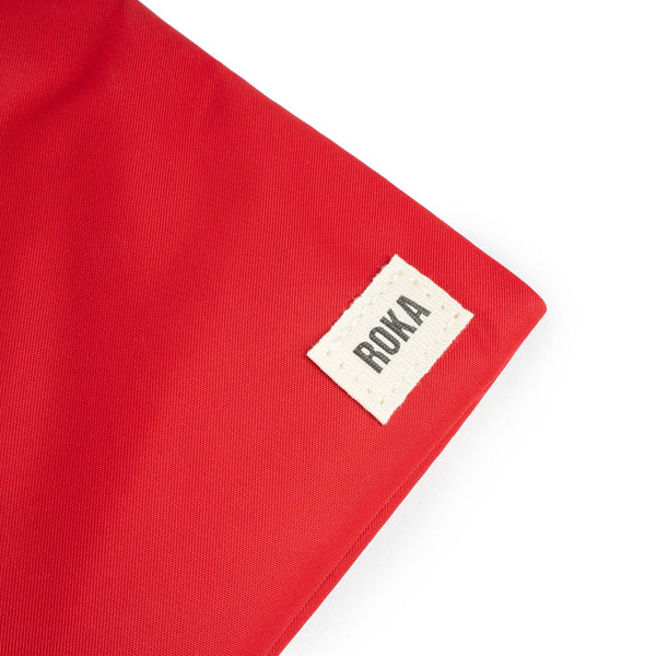 A close up photo of the bottom corner of a red bag, showing the ROKA London label.