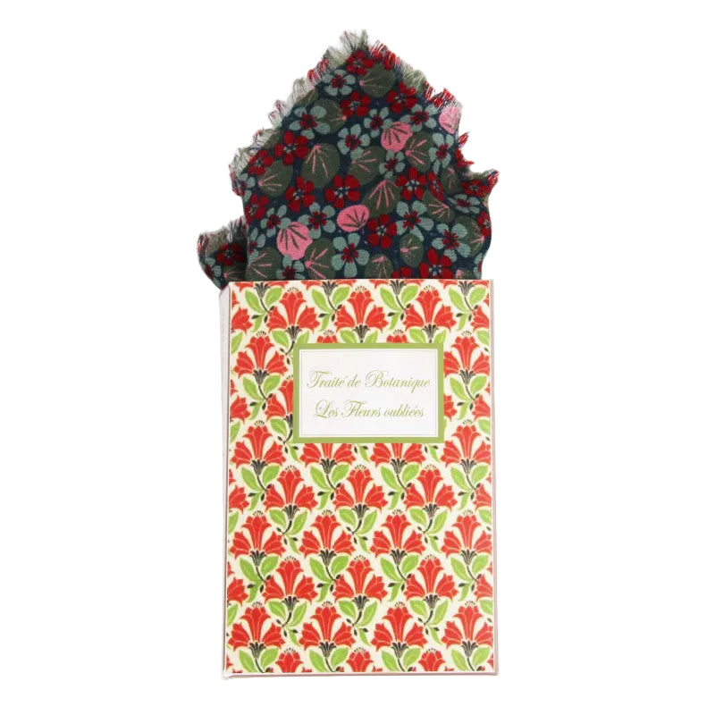 A folded patterned pocket square is displayed above its matching printed presentation box on a clean white background. The pocket square has a dark charcoal base with red, pink, and green floral motifs, and the box features a repeating red and green floral pattern with a central label reading 'Fleur de Balincourt La Fleur courtoise'.