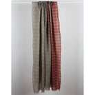 Two long patterned fabric panels hanging side by side against a plain light gray background. The left panel is taupe with a circular spiral pattern, and the right panel is rust red with a repeating geometric circle motif.