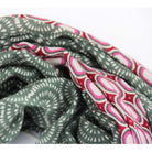 A close-up of a patterned fabric or scarf with two distinct designs: one side features a sage green and white geometric wave pattern, while the other side displays a red, pink, and white paisley-like pattern.