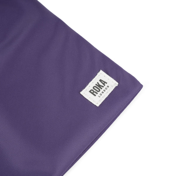 A close up photo of the bottom corner of a purple bag, showing the ROKA London label.