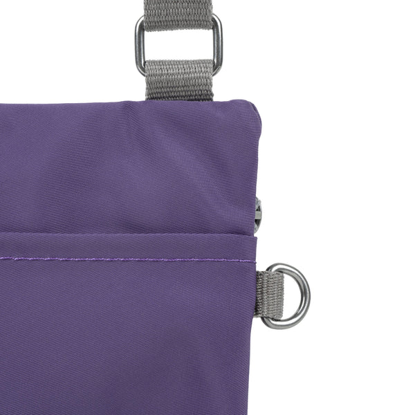 A close up photo of the back of a purple bag, showing the grey strap and neatly stitched pocket opening.