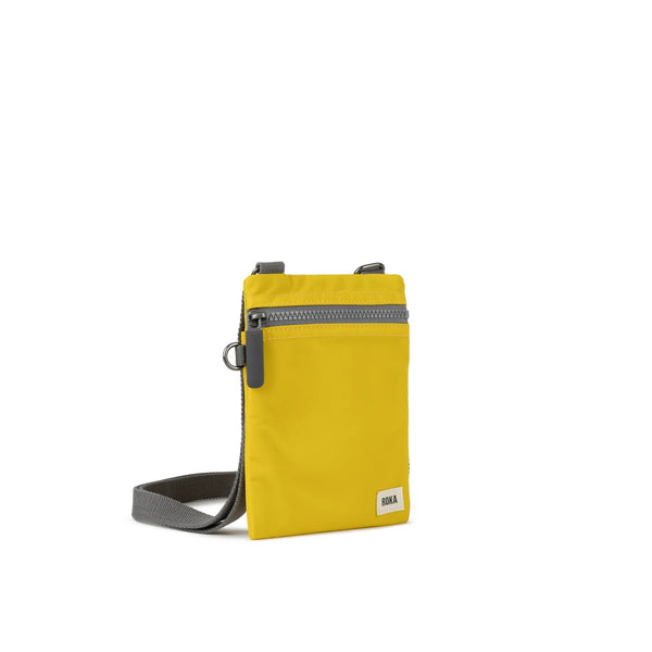 A photo of the front and side of a small rectangular yellow pocket bag. It has a grey zip horizontally at the top, grey straps, and a small ROKA logo in the bottom right corner. 