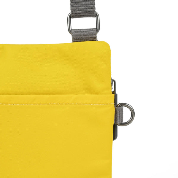  close up photo of the back of a yellow bag, showing the grey strap and neatly stitched pocket opening.