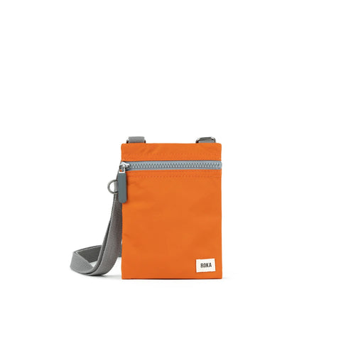 A photo of the front of a small rectangular orange pocket bag. It has a grey zip horizontally at the top, grey straps, and a small ROKA logo in the bottom right corner.