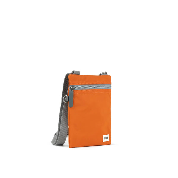 A photo of the front and side of a small rectangular orange pocket bag. It has a grey zip horizontally at the top, grey straps, and a small ROKA logo in the bottom right corner. 