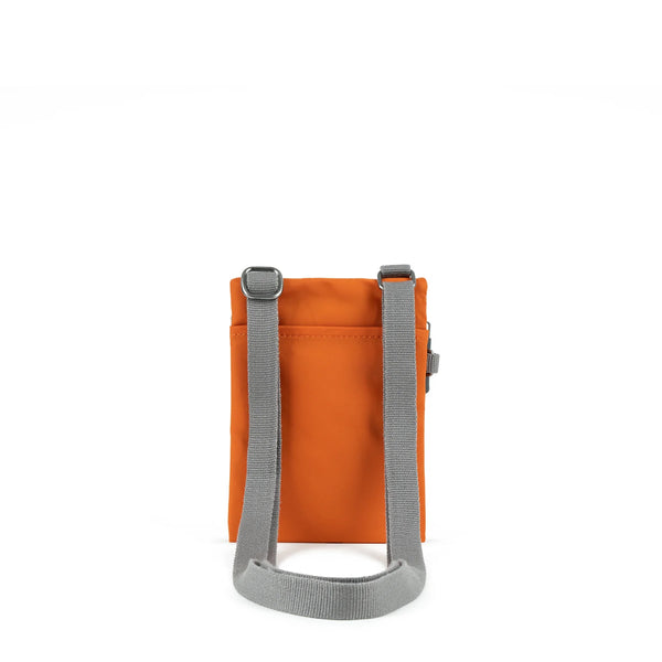 A photo of the back of a small rectangular orange pocket bag. It has a pocket and grey straps.