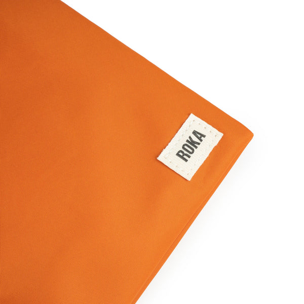 A close up photo of the bottom corner of an orange bag, showing the ROKA London label.