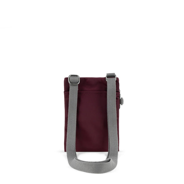 A photo of the back of a small rectangular dark plum coloured pocket bag. It has a pocket and grey straps.