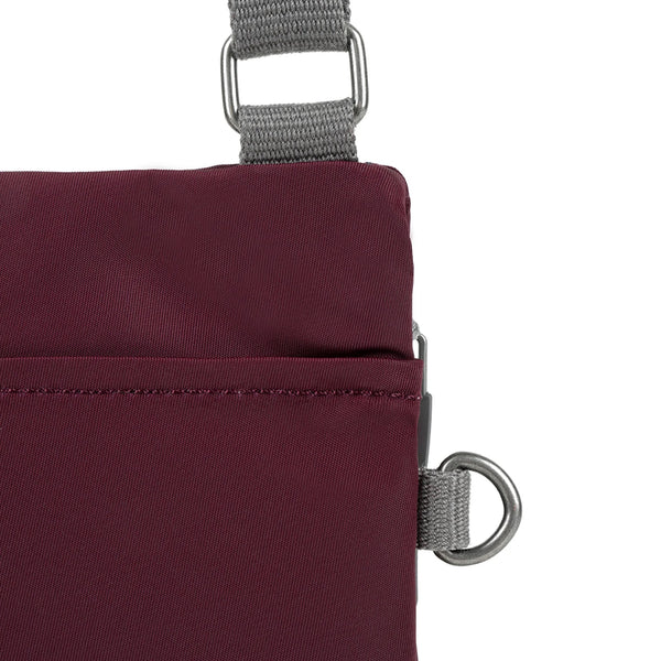 A close up photo of the back of a dark plum coloured bag, showing the grey strap and neatly stitched pocket opening.