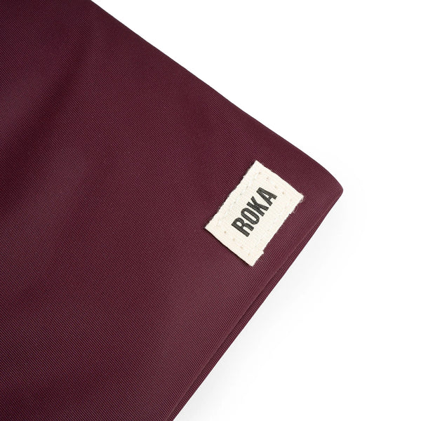 A close up photo of the bottom corner of a dark plum coloured bag, showing the ROKA London label.