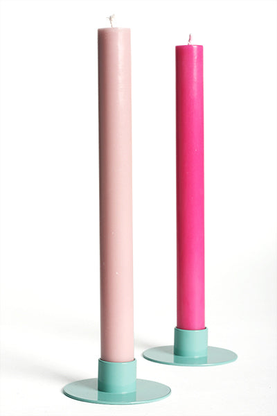 Two pink candles on turquoise candle holders against a white background