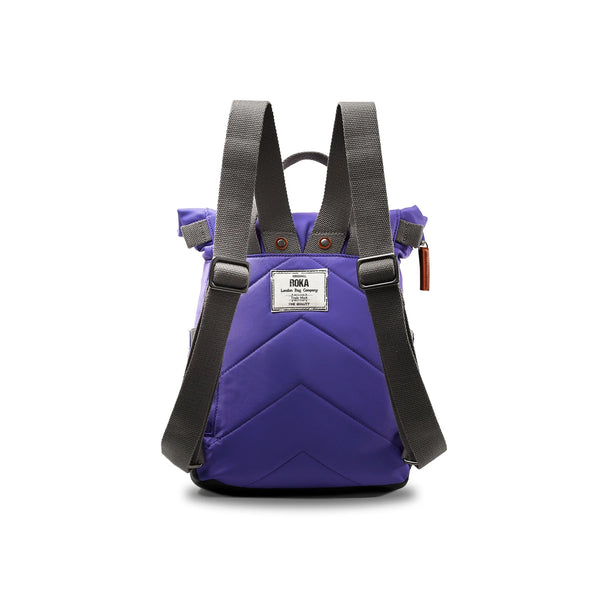 Photo showing the back of a small purple coloured backpack. The straps and handles are grey and there’s a small fabric label with the ROKA logo on.