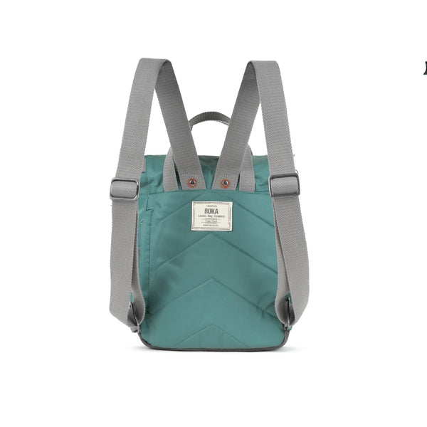 Photo showing the back of a small sage green coloured backpack. The straps and handles are grey and there’s a small fabric label with the ROKA logo on.