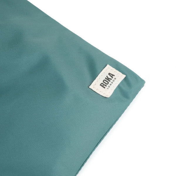 A close up photo of the bottom corner of a sage green bag, showing the ROKA London label.