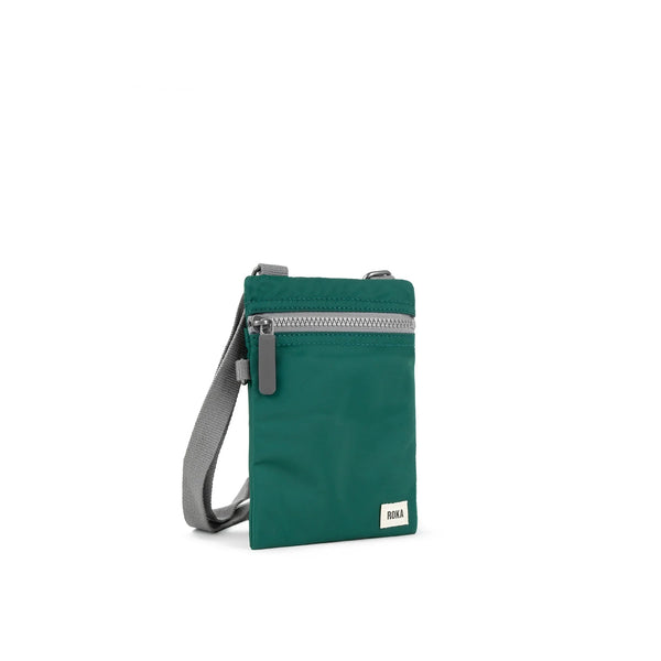 A photo of the front and side of a small rectangular teal pocket bag. It has a grey zip horizontally at the top, grey straps, and a small ROKA logo in the bottom right corner.