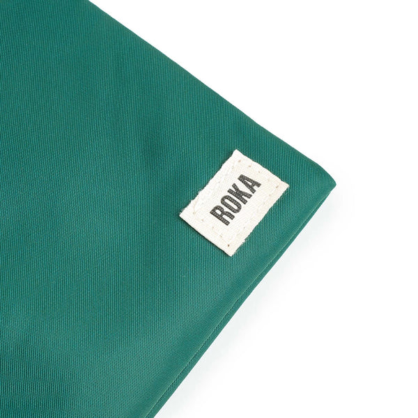A close up photo of the bottom corner of a teal bag, showing the ROKA London label.