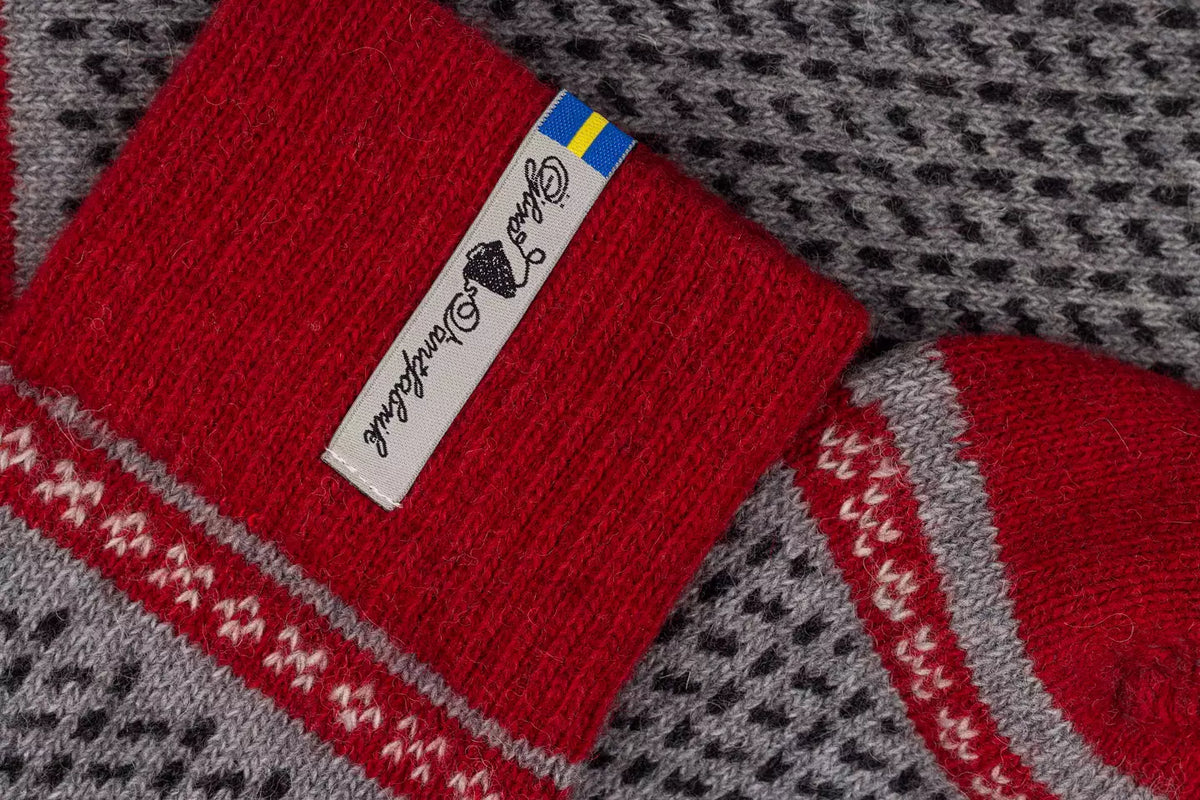 Close-up of a red knit sock with a white brand tag  and a small Swedish flag, laid over a gray and black patterned knit textile.