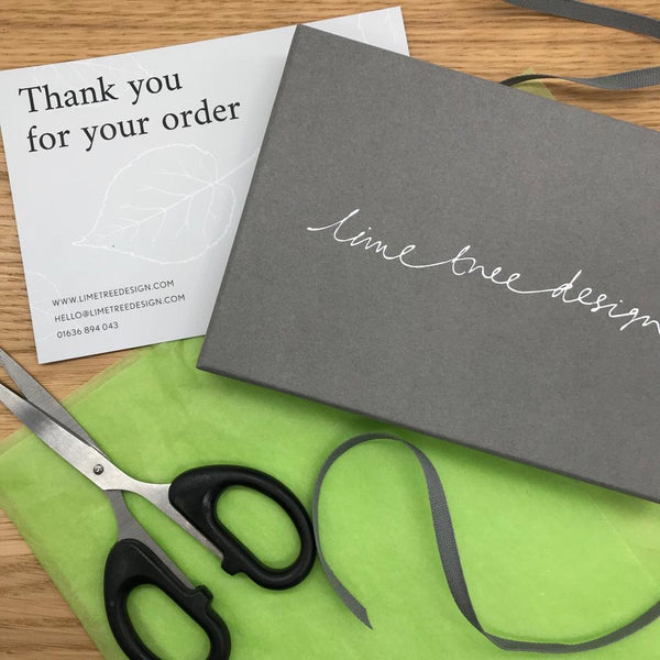 Photo of scissors, green tissue paper, ribbon and a grey gift box, with a 'Thank you for your order' card