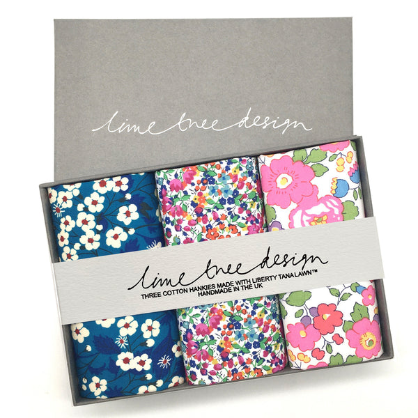 A grey box with three folded hankies inside. One is blue with white and red flowers, one has small pink, blue, green and yellow flowers against a white background, and the last has pink flowers with green leaves and yellow accents against a white background.