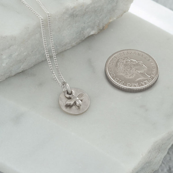 mini bee necklace next to coin for size 